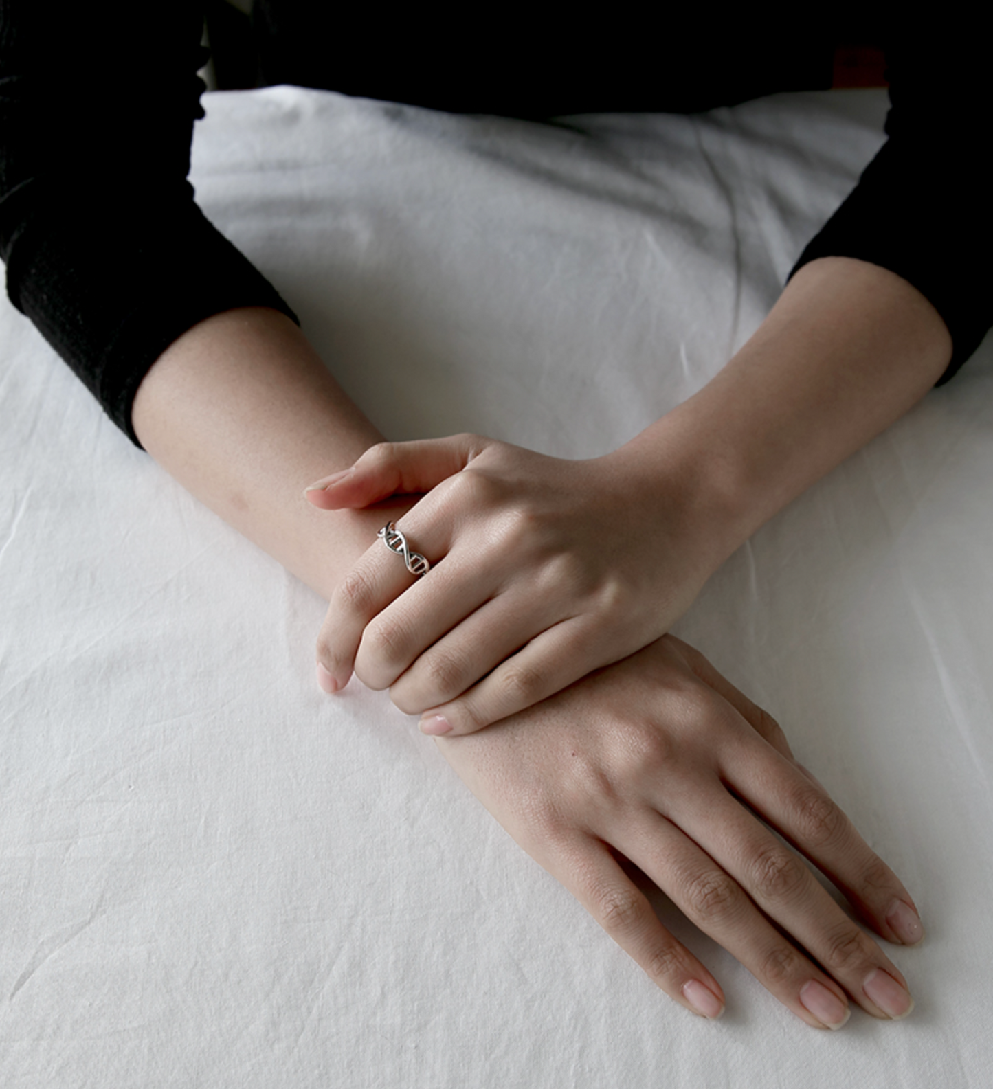 Two hands resting together while wearing a sterling silver DNA double-helix ring