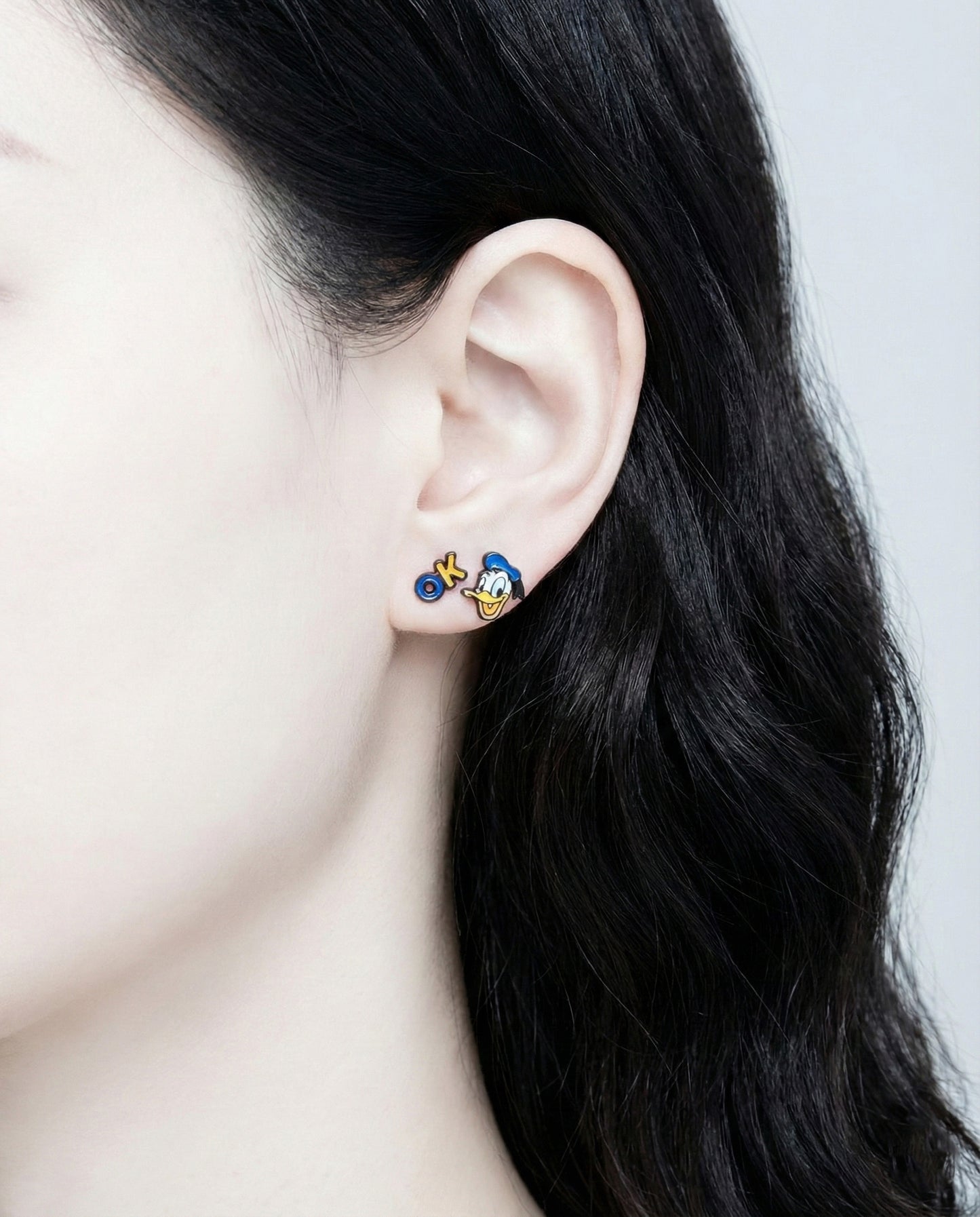 Woman wearing Donald Duck and OK sign enamel stud earrings - side profile showing cute character jewelry