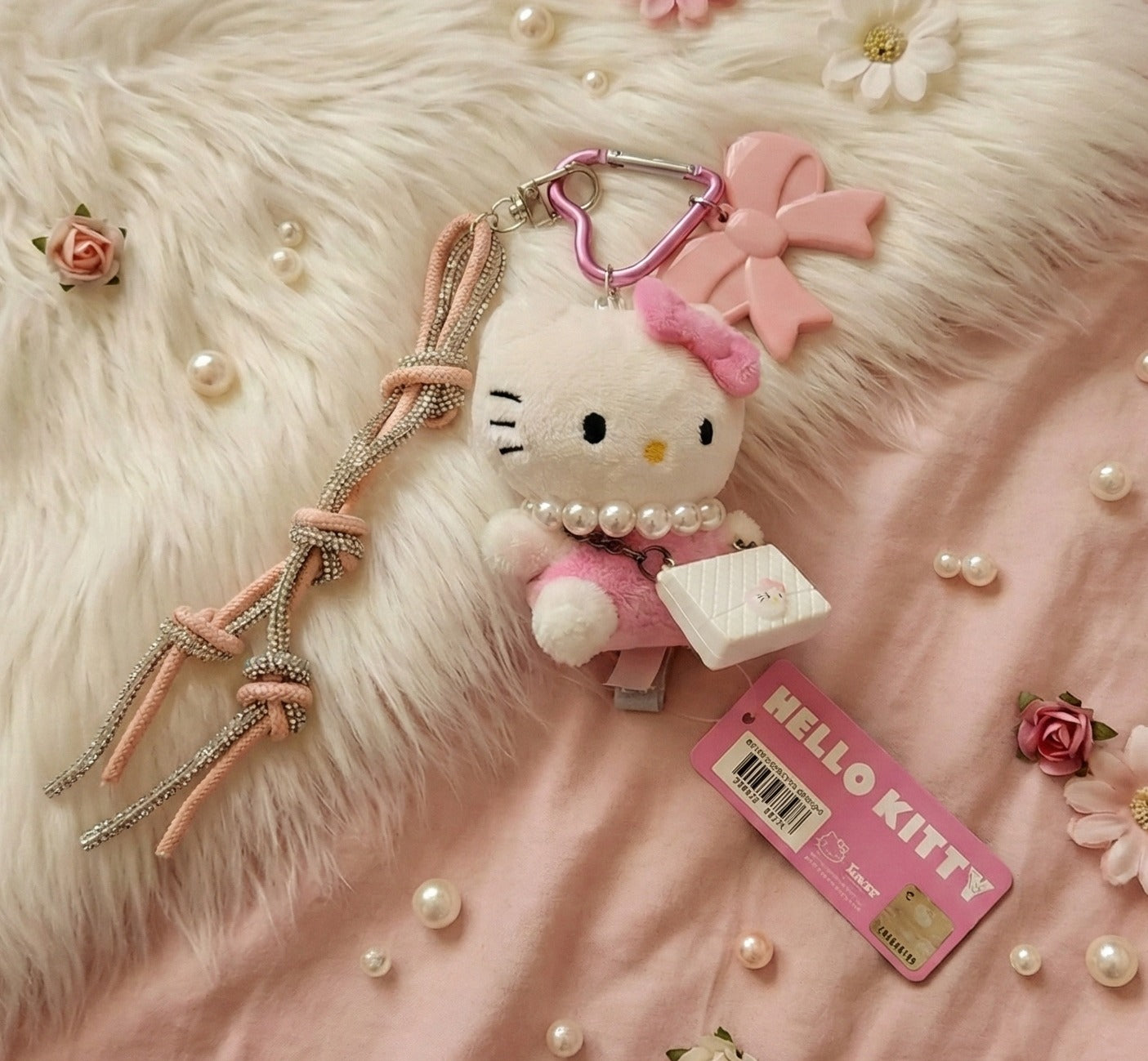 Flat lay of Hello Kitty plush keychain with pearls and roses on pink fur background — coquette gift aesthetic