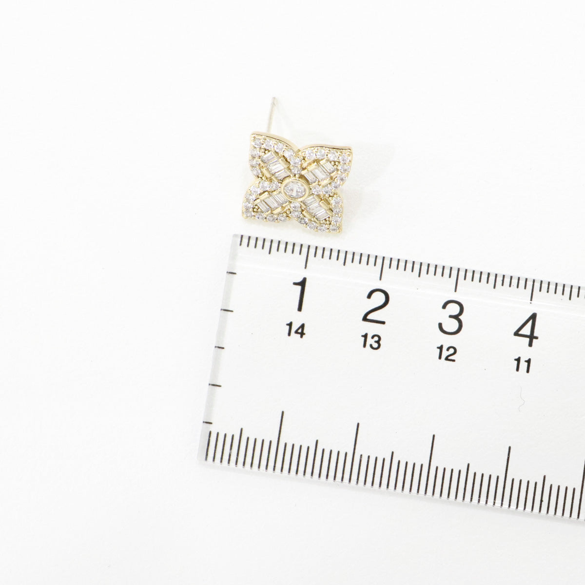 Size comparison of gold baguette flower stud earrings with measuring ruler showing 1cm width