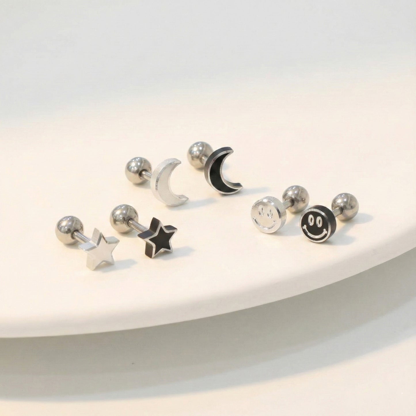 Surgical steel moon star smiley face piercing studs in silver and black on white surface