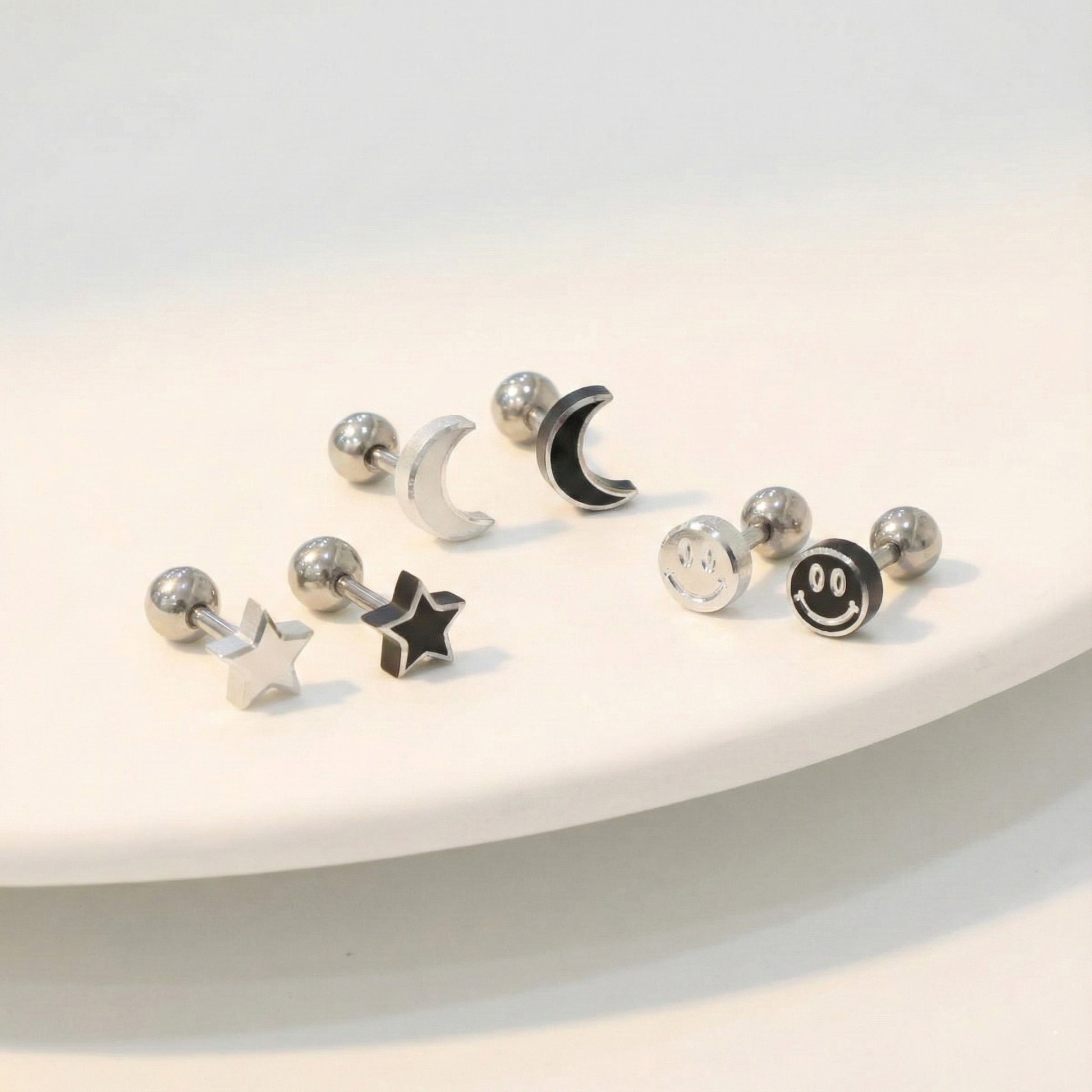 Surgical steel moon star smiley face piercing studs in silver and black on white surface
