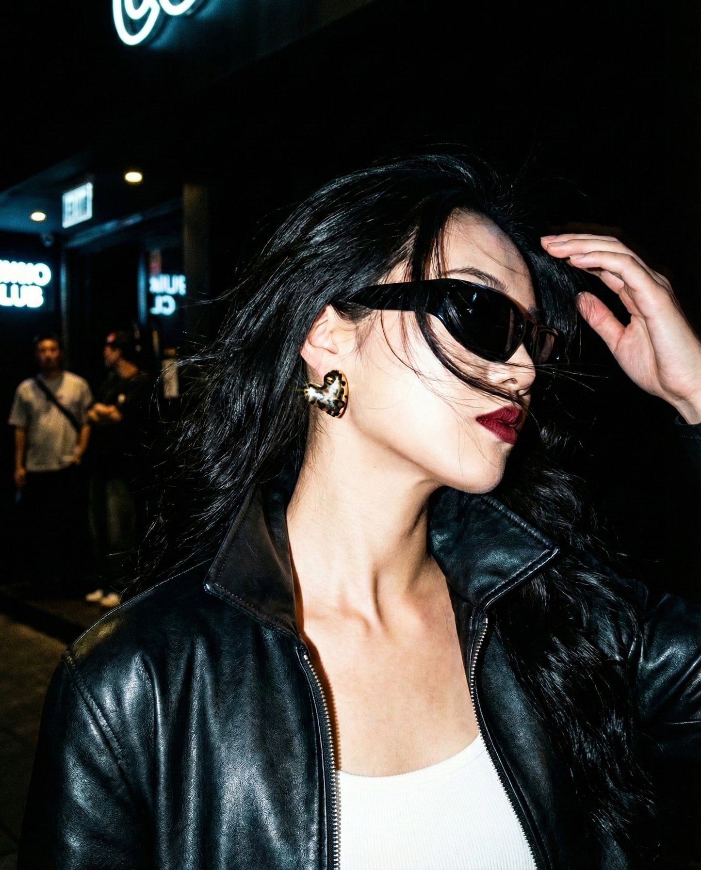 Woman wearing leopard print heart earrings with leather jacket and sunglasses at night