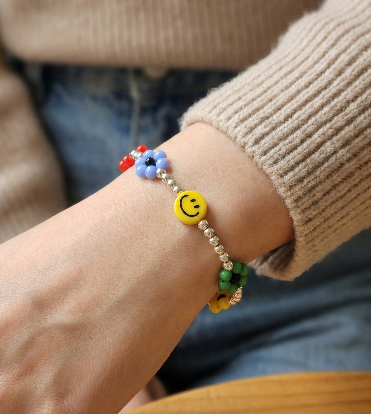 Smiley garden flower bead bracelet and white Hug Me bear bracelet stacked on wrist — friendship bracelet styling