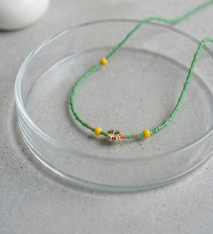 Green seed bead necklace with gold four-leaf clover charm and yellow accent beads displayed on glass plate