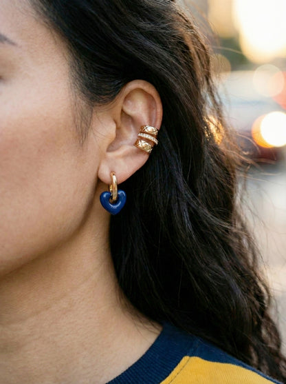 Close-up of woman's ear wearing navy blue puffy heart earrings with gold ear cuff styling