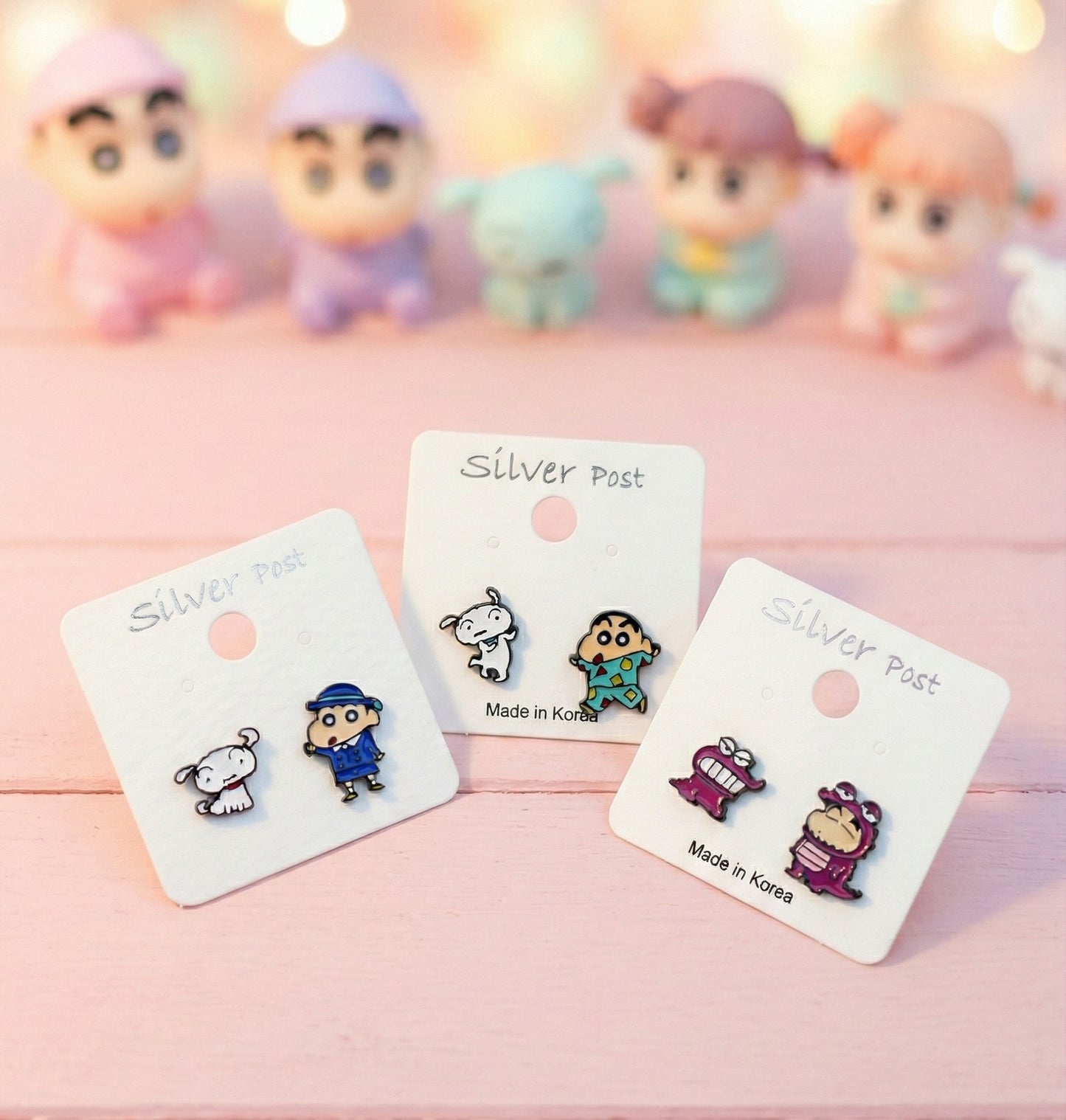 Three pairs of Crayon Shin-chan asymmetrical stud earrings displayed on white cards with silver post labels, featuring school uniform, pajamas, and Chocobi dinosaur designs