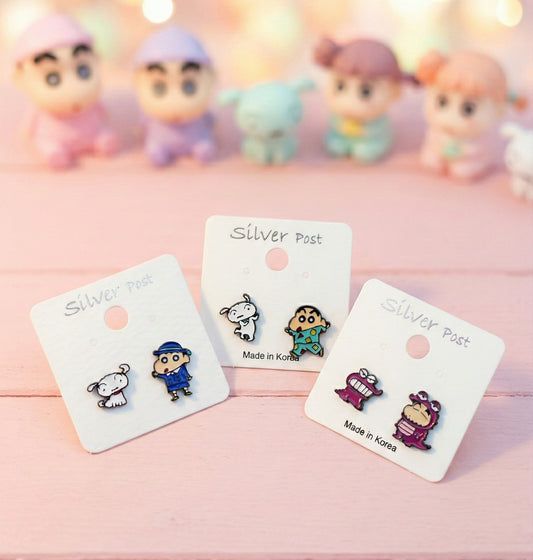 Three pairs of Crayon Shin-chan asymmetrical stud earrings displayed on white cards with silver post labels, featuring school uniform, pajamas, and Chocobi dinosaur designs