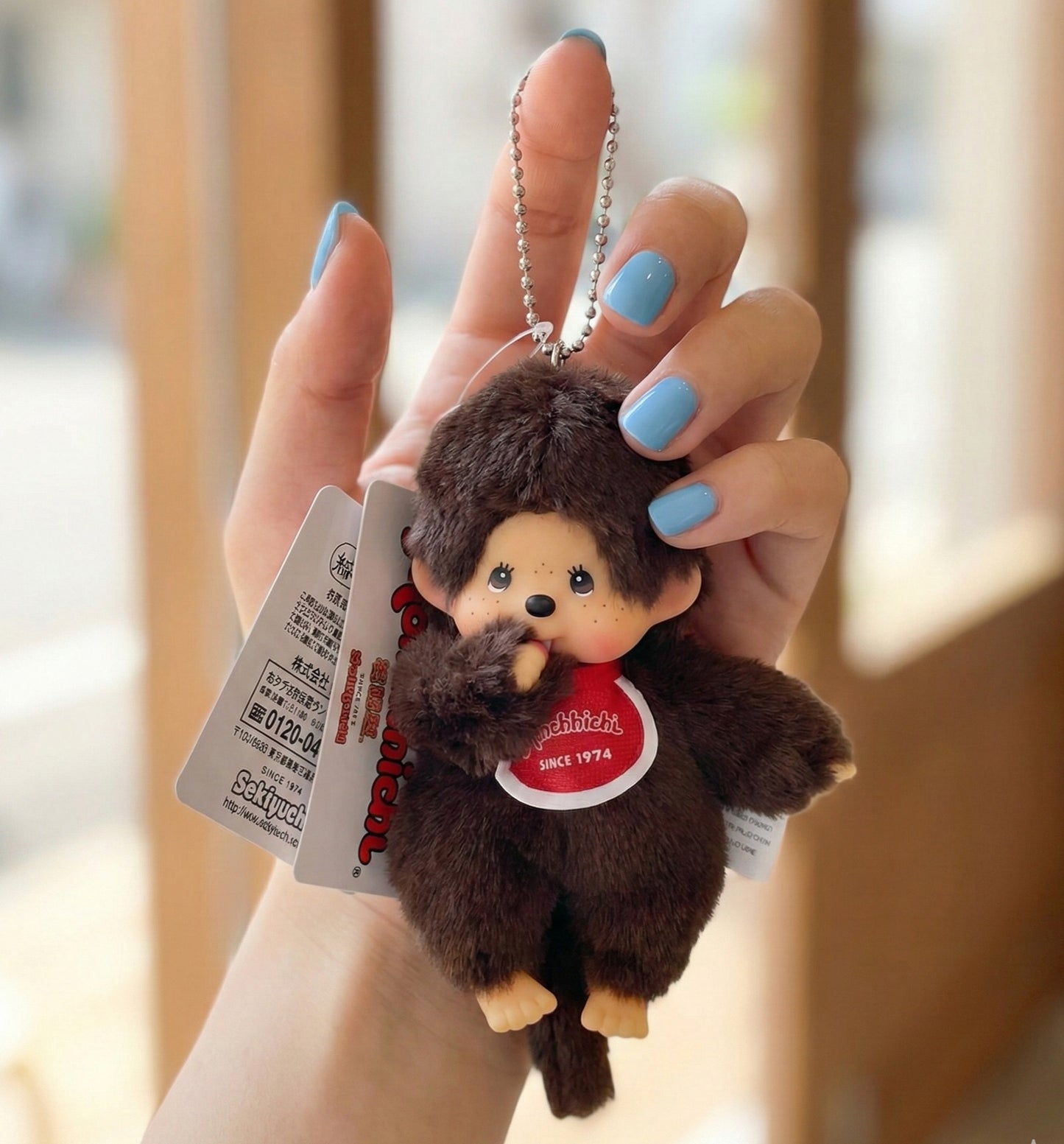 Hand holding Monchhichi Classic Boy plush keychain with blue nail polish showing size reference — vintage Y2K kawaii accessory