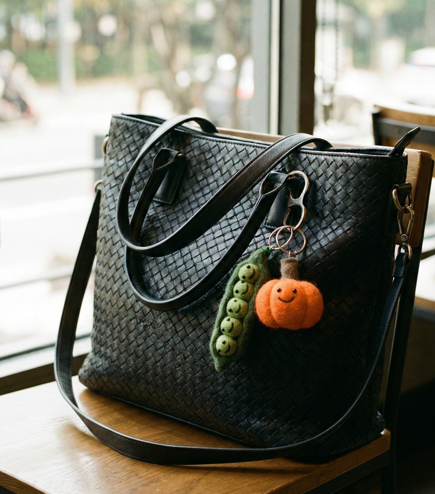 Felt vegetable keychains on black woven handbag at cafe