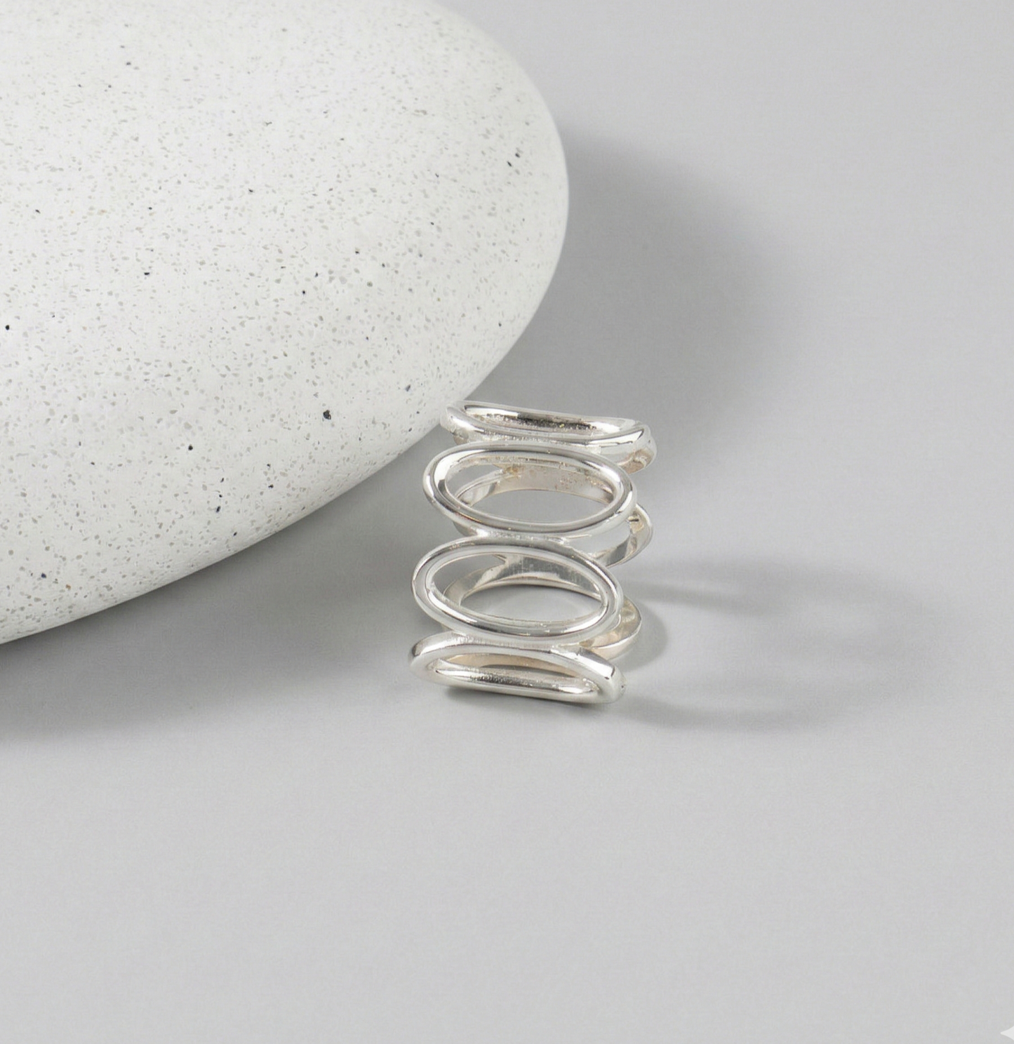 925 sterling silver oval loop wide band ring standing upright against white stone on gray background, showing continuous oval link structure from front angle