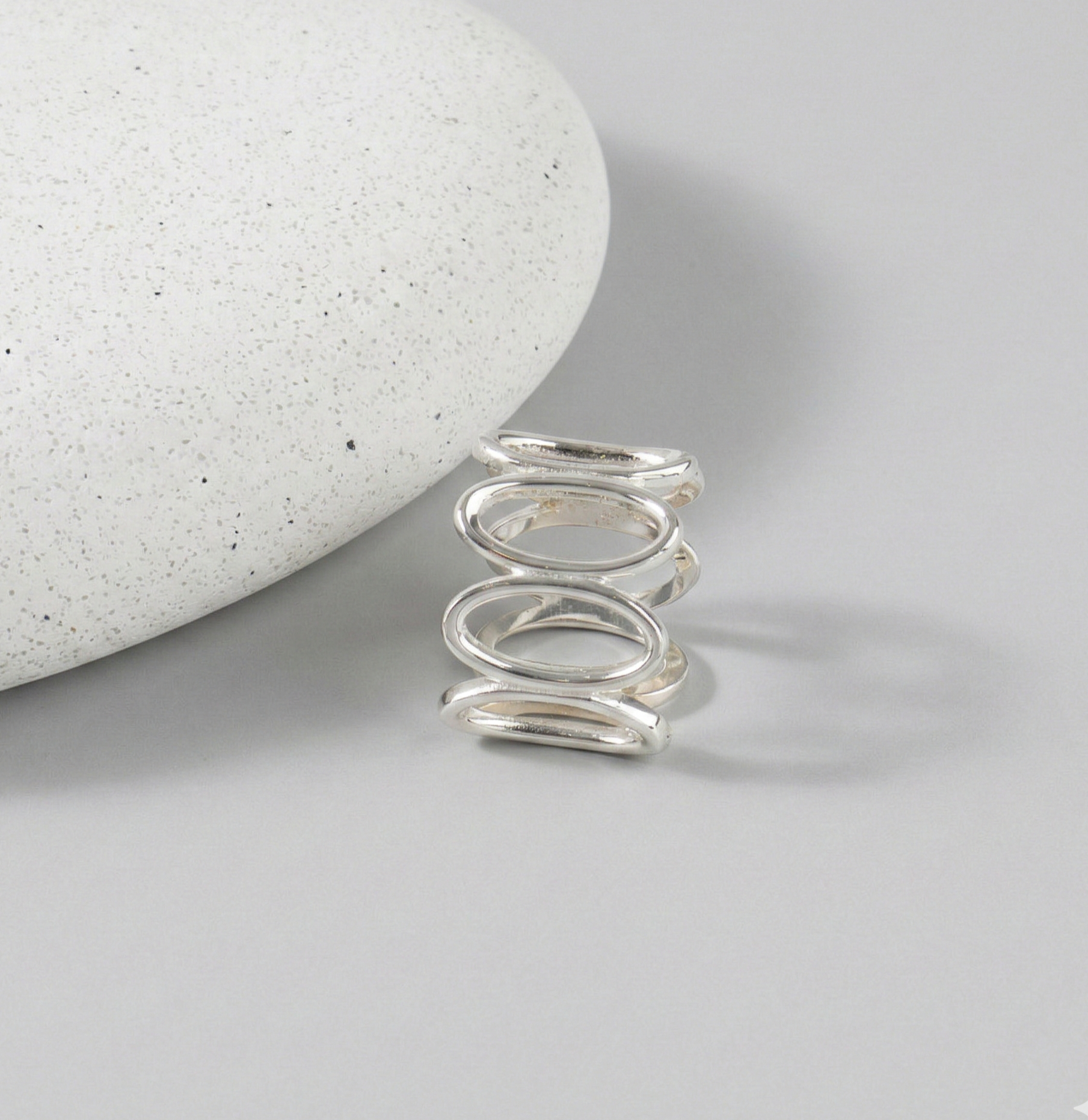 925 sterling silver oval loop wide band ring standing upright against white stone on gray background, showing continuous oval link structure from front angle