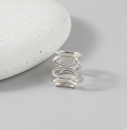 925 sterling silver oval loop wide band ring standing upright against white stone on gray background, showing continuous oval link structure from front angle