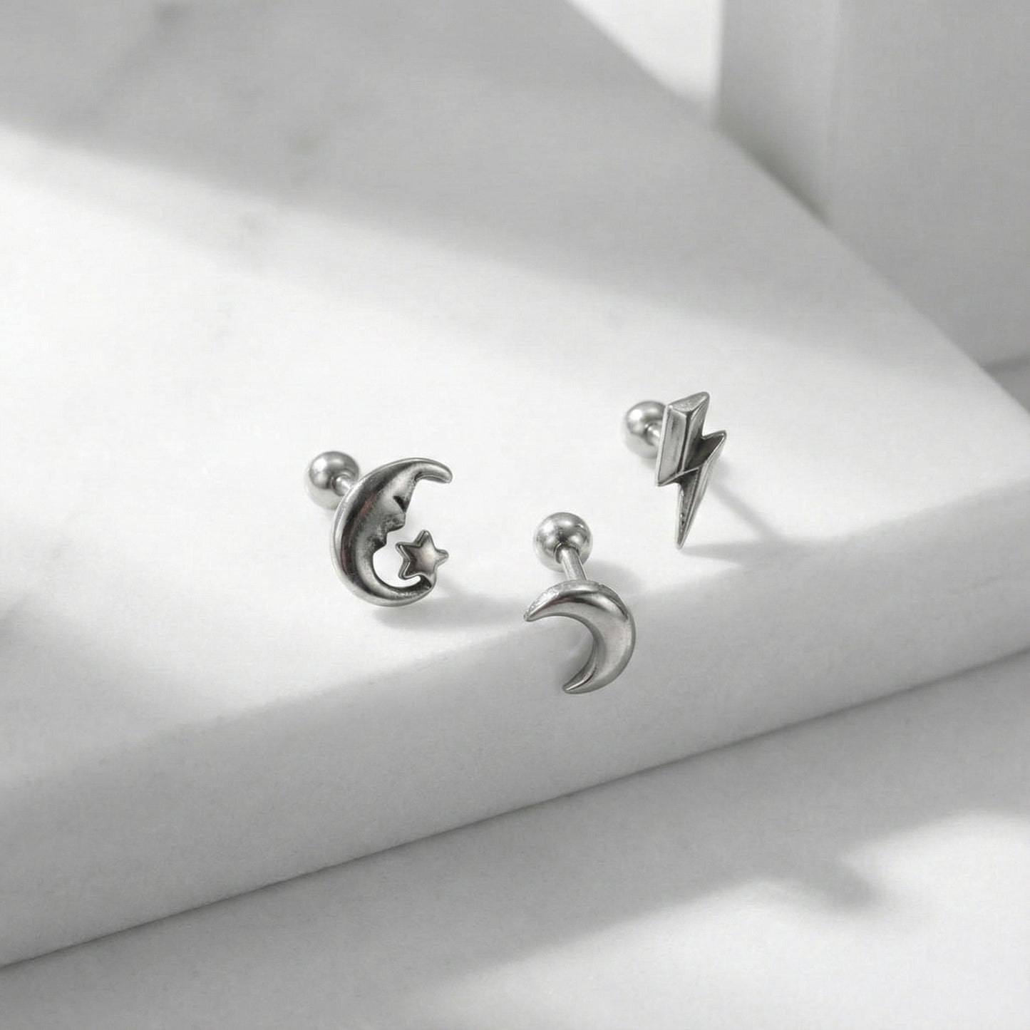 Detail shot of surgical steel celestial barbell studs with shadow - moon, crescent, lightning