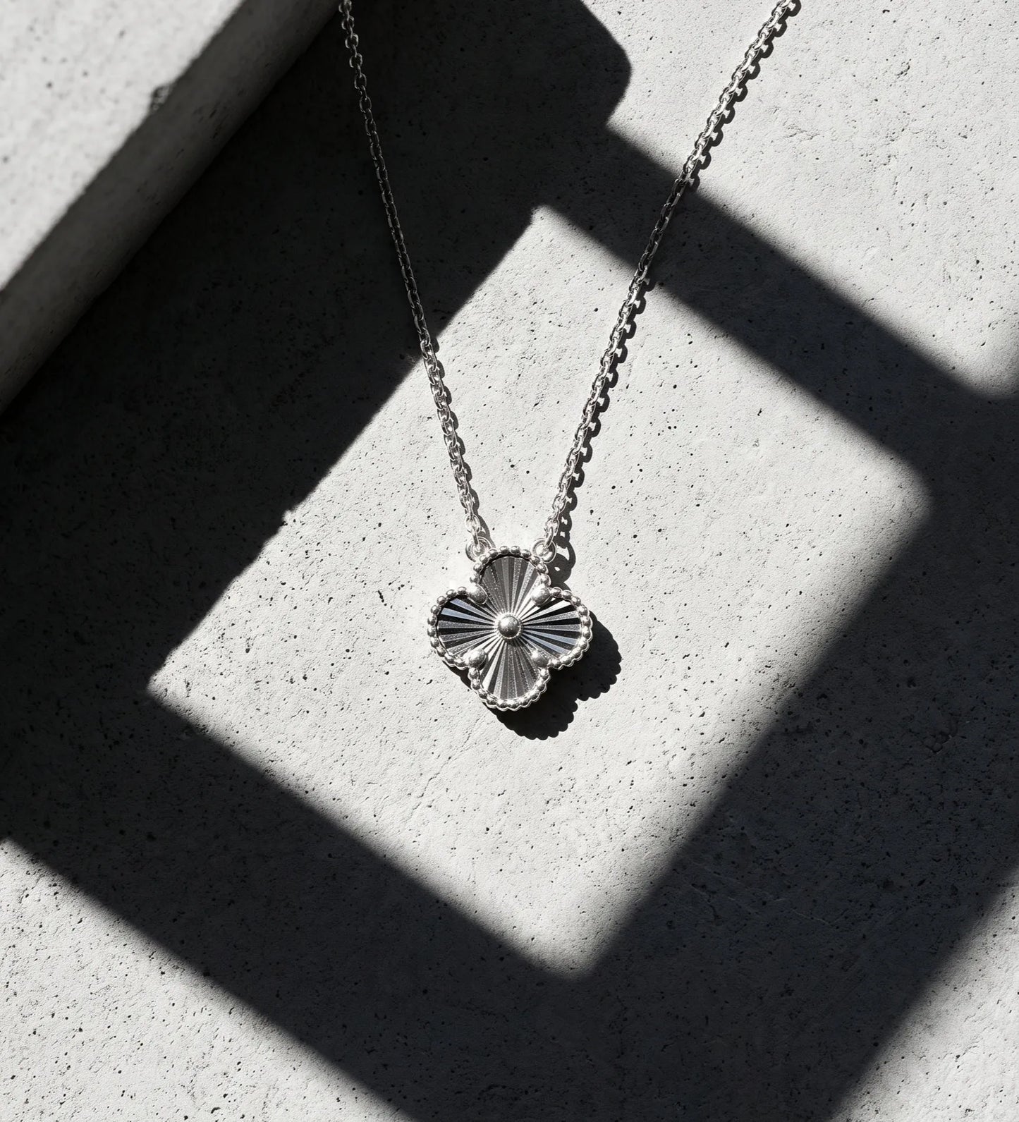 925 sterling silver milgrain four leaf clover necklace platinum plated tarnish-free, hypoallergenic K-jewelry daily pendant shadow editorial shot.
