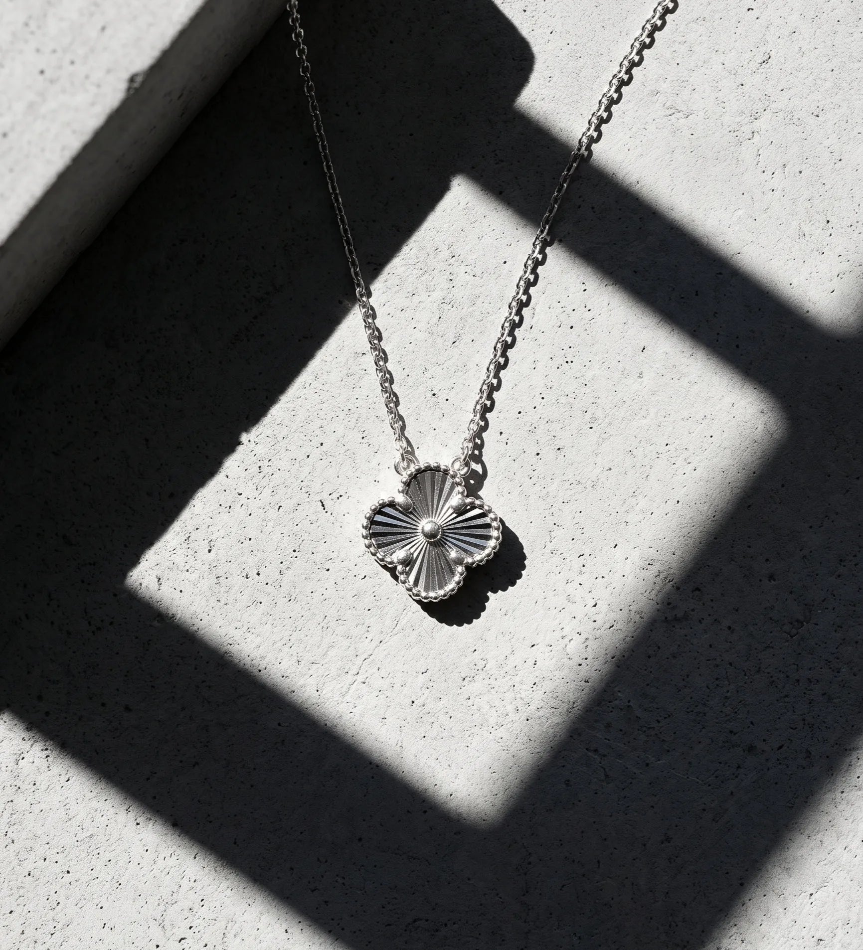 925 sterling silver milgrain four leaf clover necklace platinum plated tarnish-free, hypoallergenic K-jewelry daily pendant shadow editorial shot.