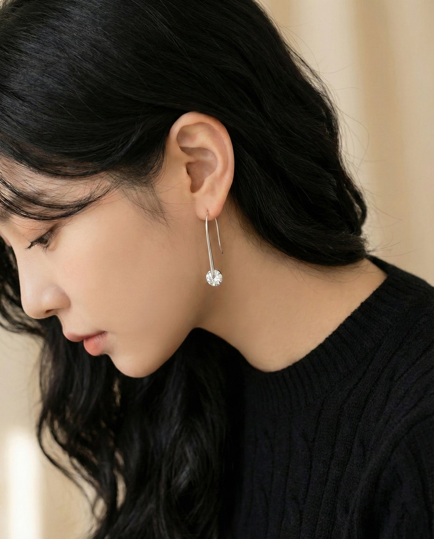 Downward angle view of woman wearing silver long drop cubic zirconia earrings with black sweater