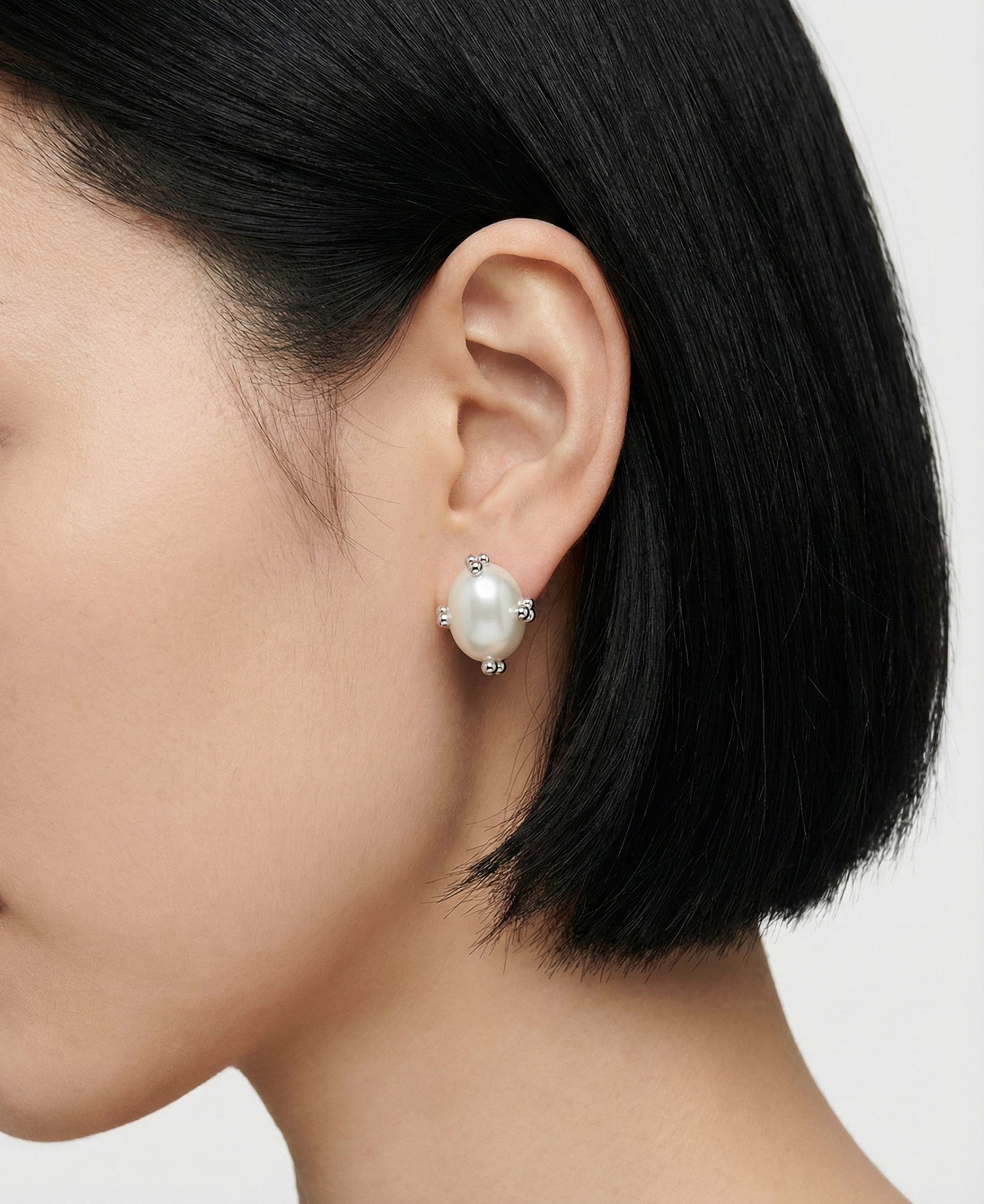 Model wearing a silver oval pearl stud earring, close-up side view.
