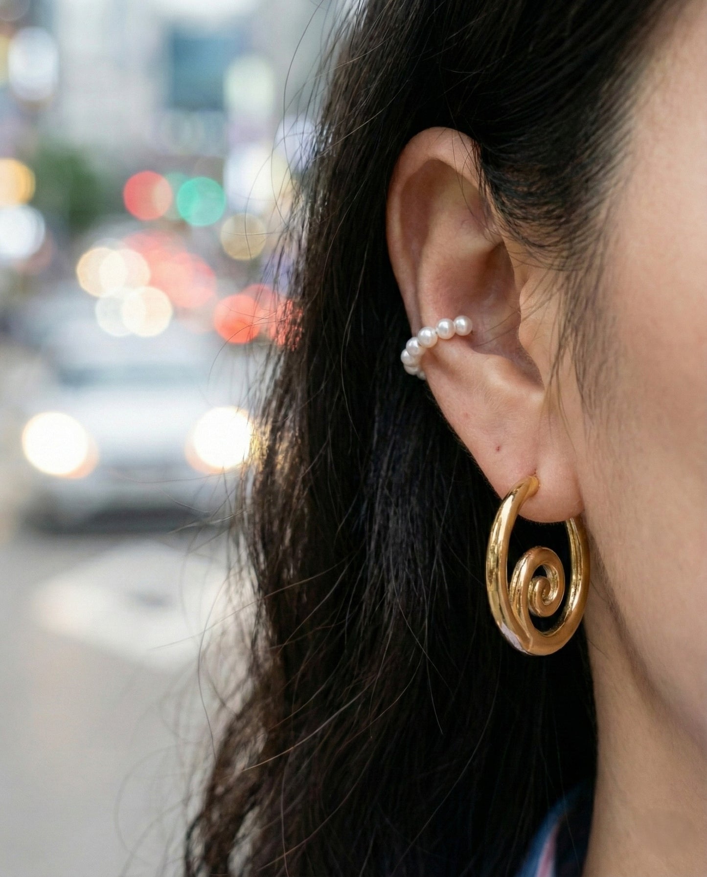Gold spiral hoop earrings with pearl ear cuff - layered jewelry look with bokeh background