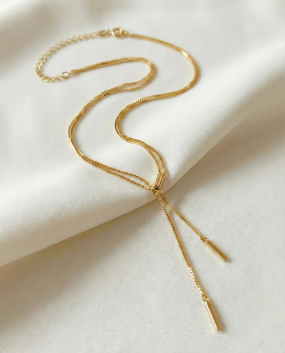 Gold double row box chain necklace with vertical stick drops, styled on soft cream fabric background