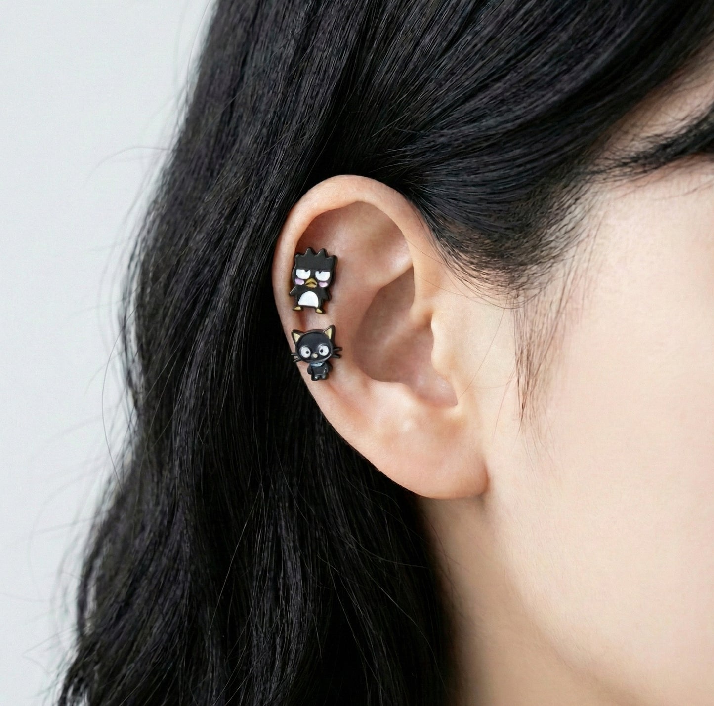  Badtz-Maru and Chococat cartilage piercings worn on helix and inner conch showing detailed enamel work 