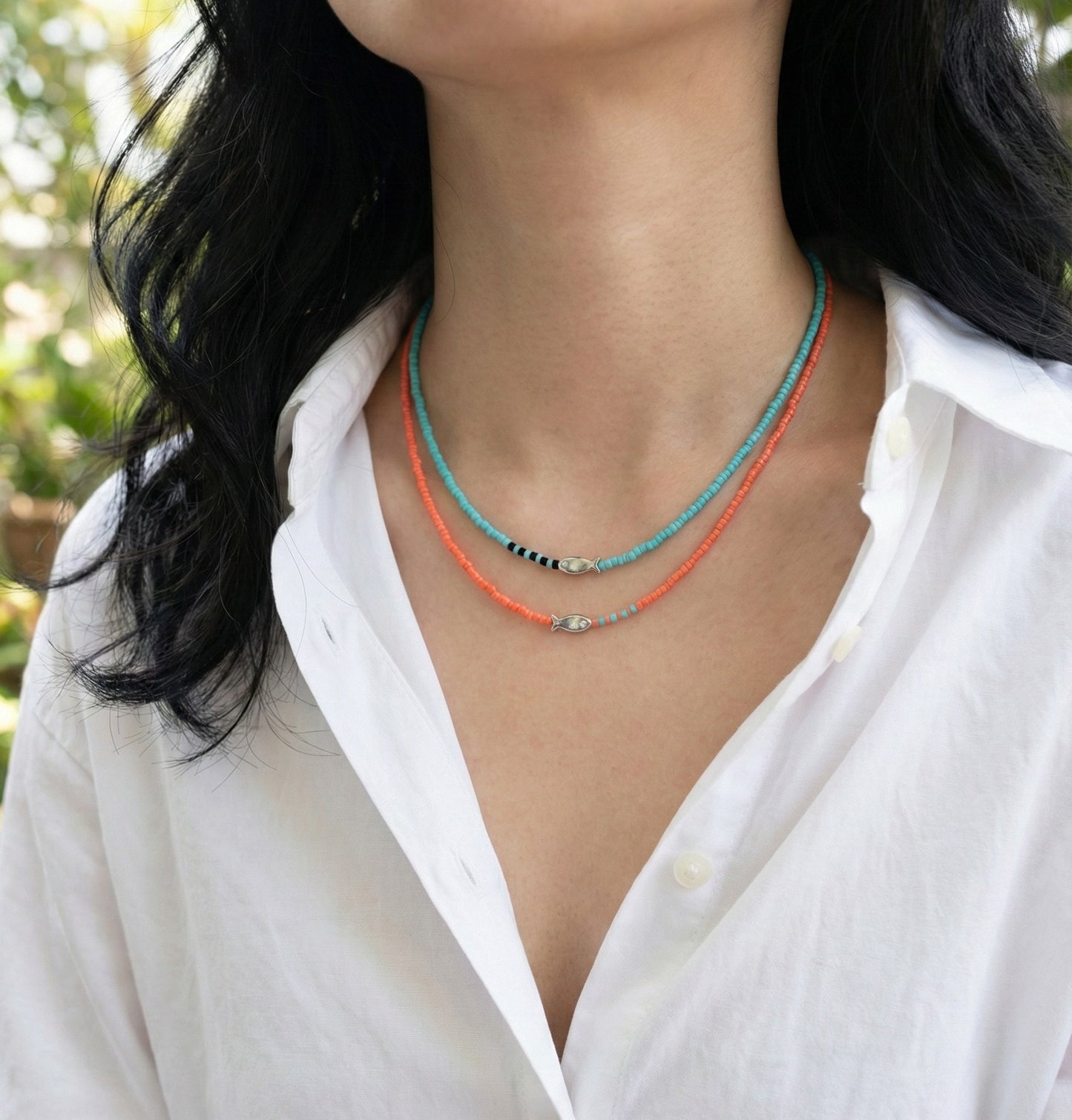 Woman wearing layered yellow and blue seed bead fish necklaces with white shirt summer styling