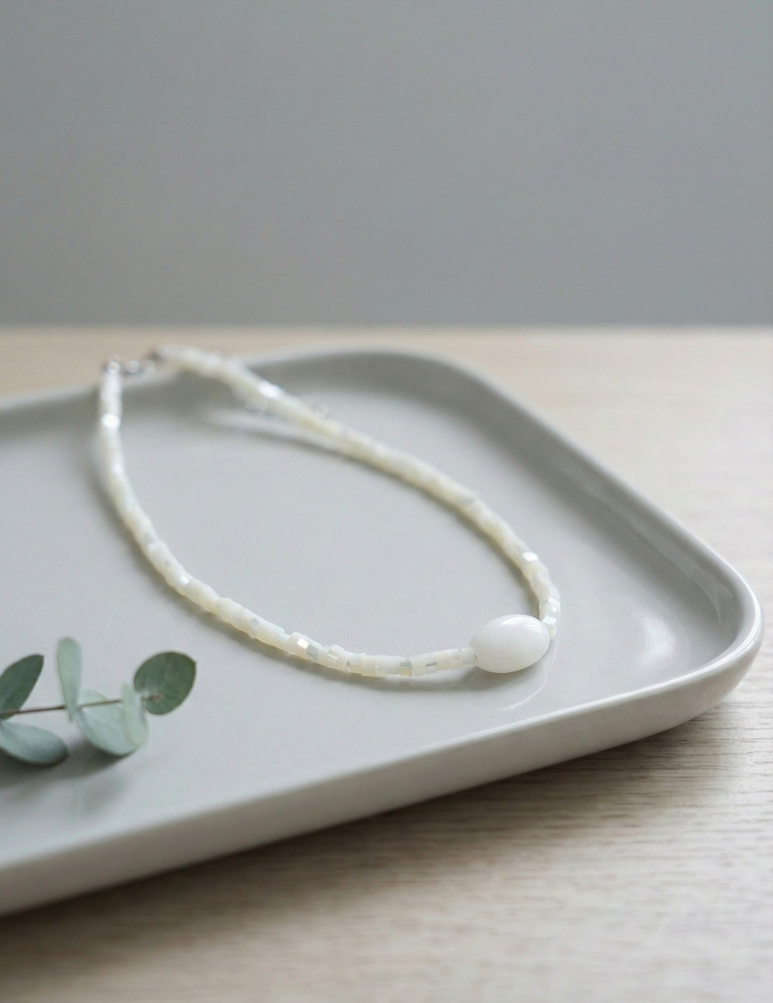 White shell heishi bead choker with pearl-like gemstone on ceramic tray"