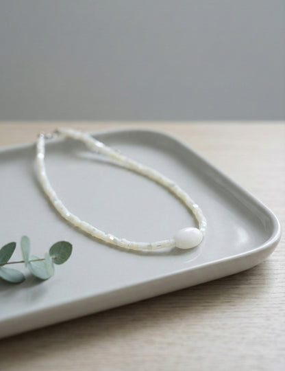 White shell heishi bead choker with pearl-like gemstone on ceramic tray"