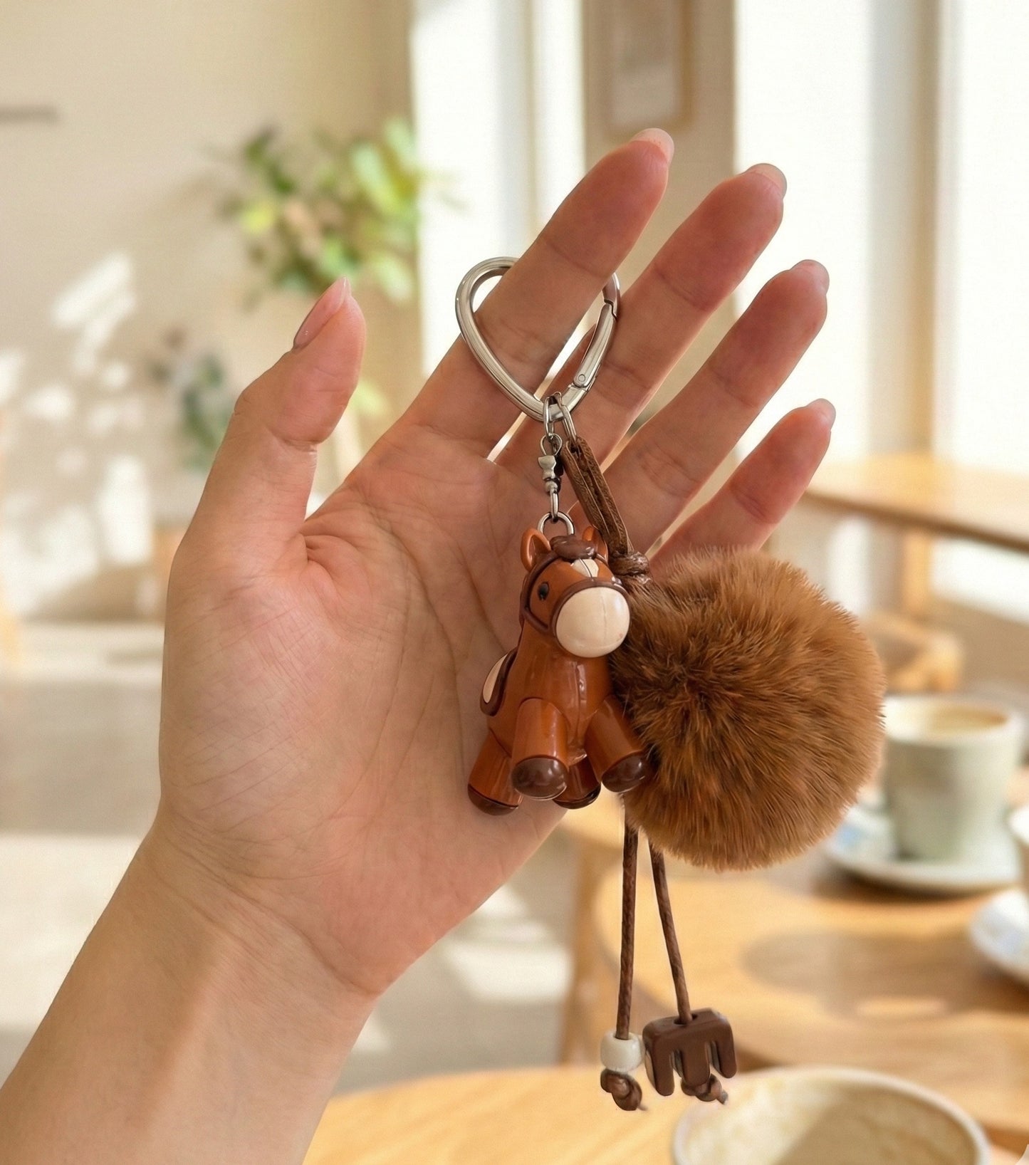 Hand holding deep brown pony keychain showing size and pompom volume