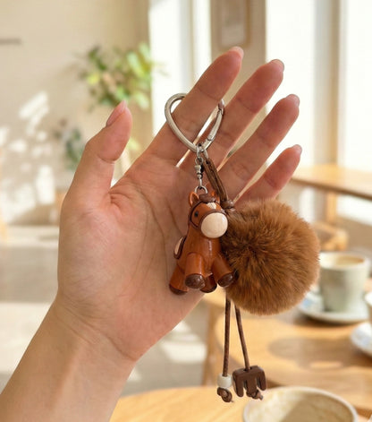 Hand holding deep brown pony keychain showing size and pompom volume