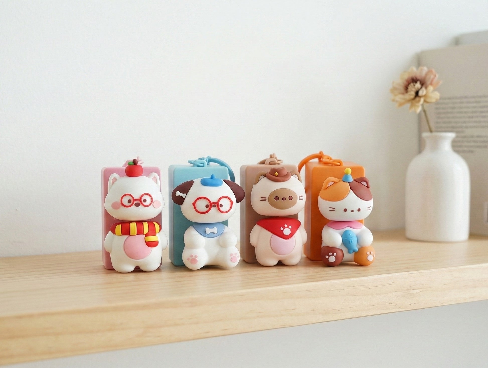 Four colorful animal keycap keychains displayed on wooden shelf with dried flower