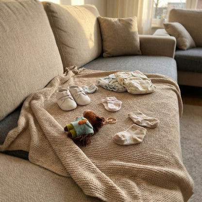 Baby shoes, socks, and a toy on a beige blanket draped over a sofa.
