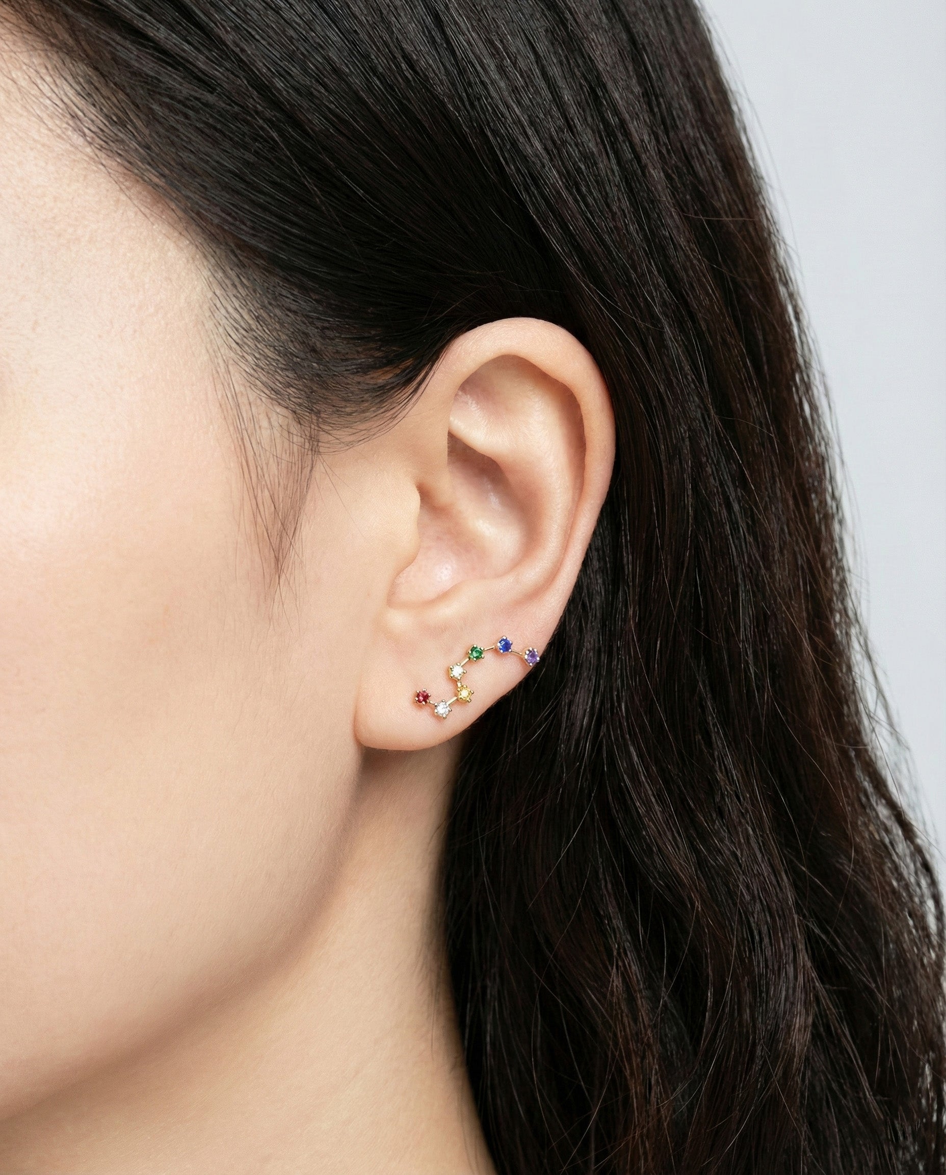 Close-up of rainbow ear climber on model ear showing colorful stones along earlobe curve