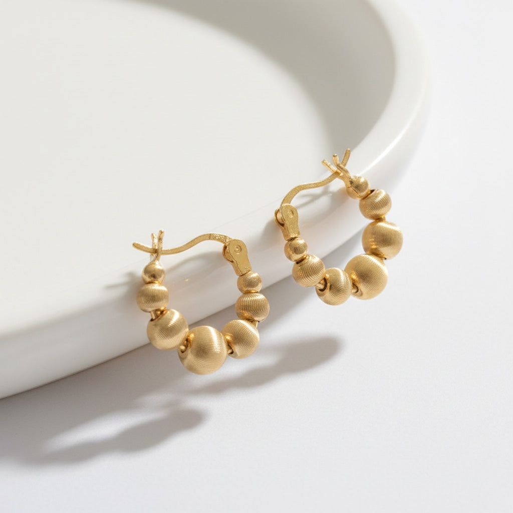 Gold textured sphere hoop earrings displayed on white ceramic plate with soft shadow, showing brushed finish bead design, gold-plated brass 925 silver posts, Korean handmade elegant minimalist jewelry gift
