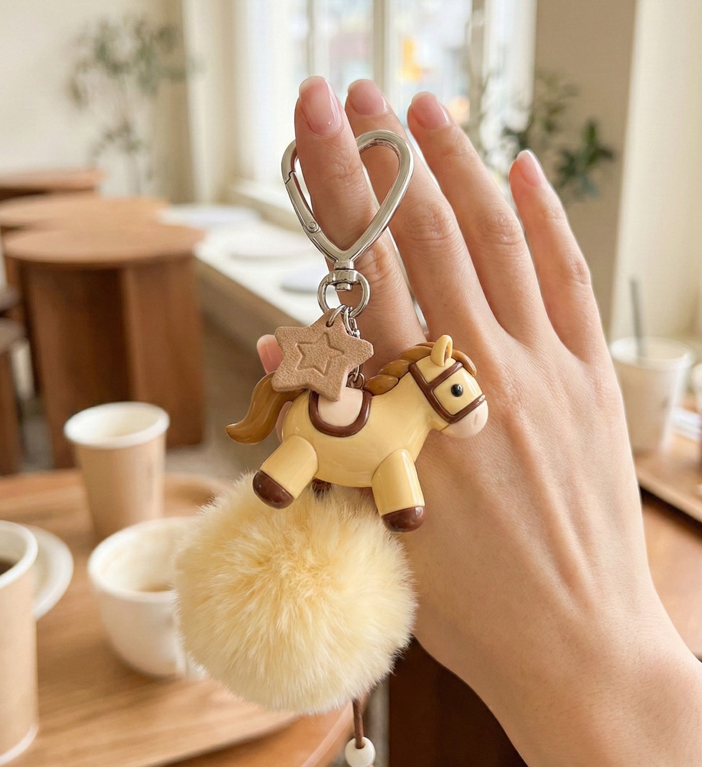 Hand holding deep brown pony keychain showing size and pompom volume