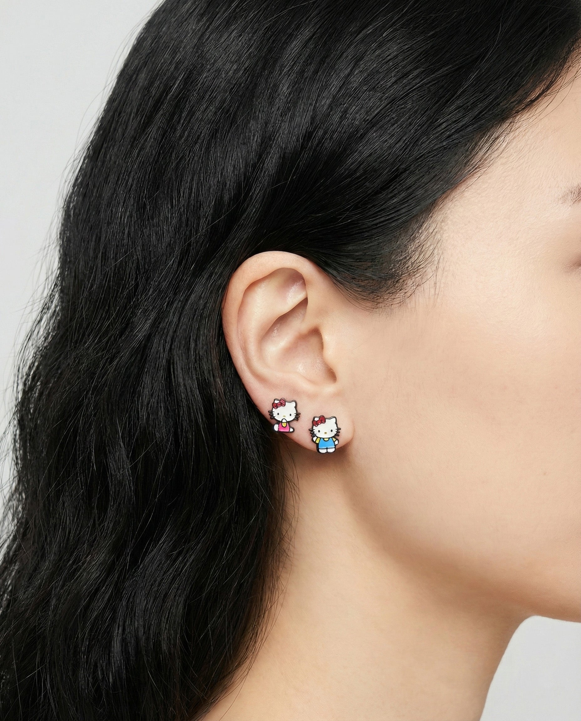 Model wearing Hello Kitty asymmetrical earrings close-up showing detailed enamel coloring and comfort fit