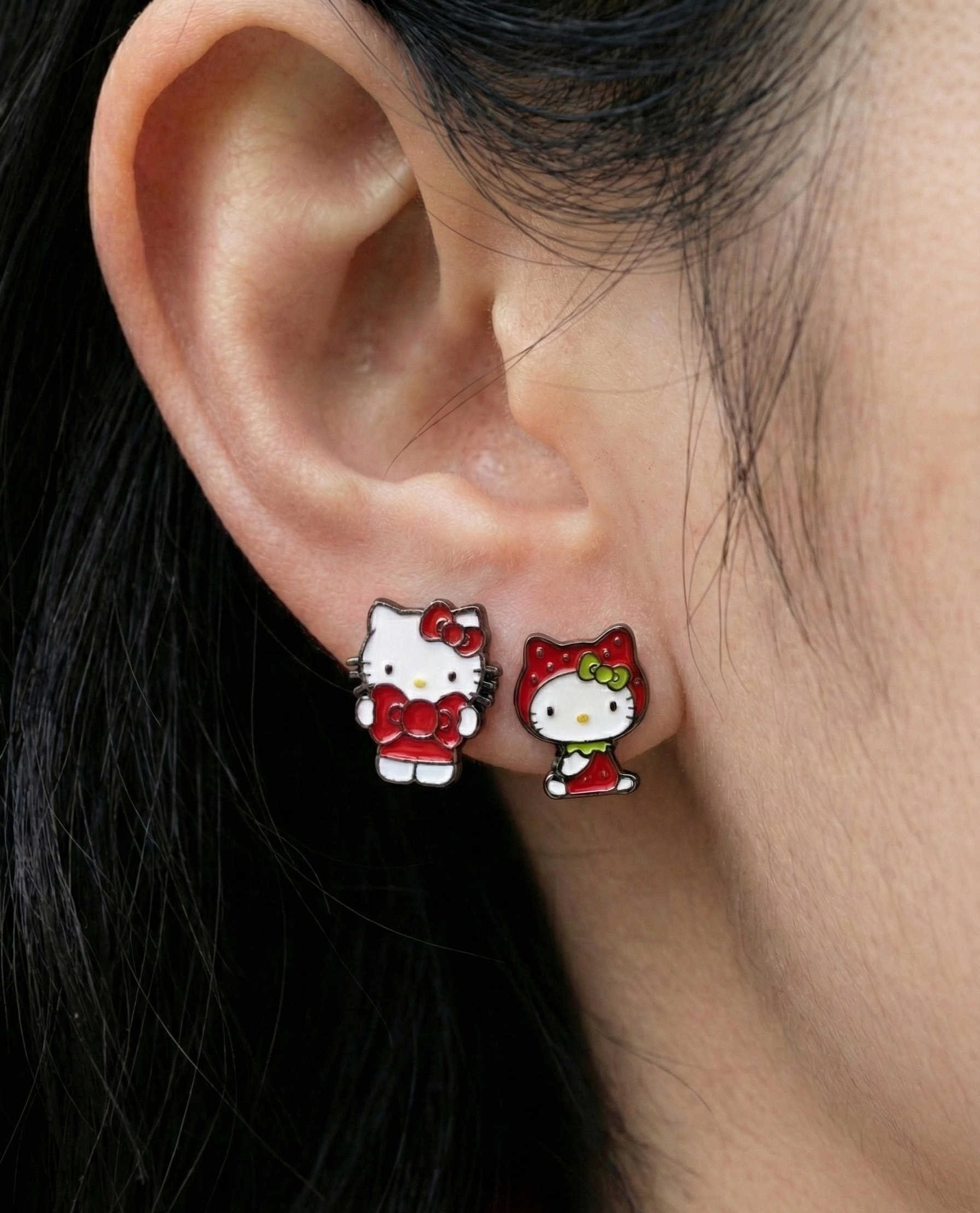 Hello Kitty earrings worn on earlobe showing asymmetric design - classic Kitty and strawberry Kitty