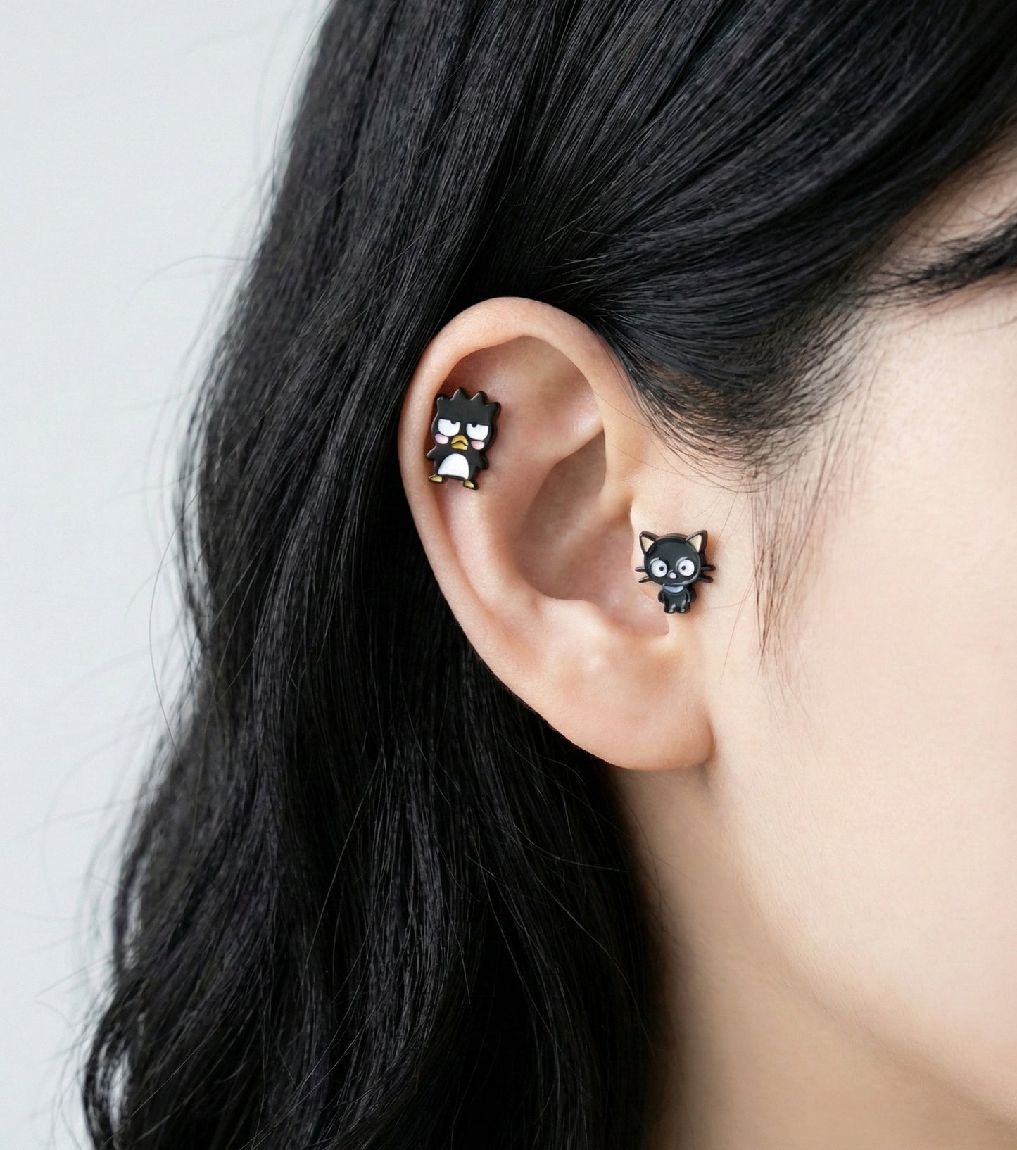 Sanrio character studs layered on ear cartilage - Badtz-Maru on helix, Chococat on lobe piercing