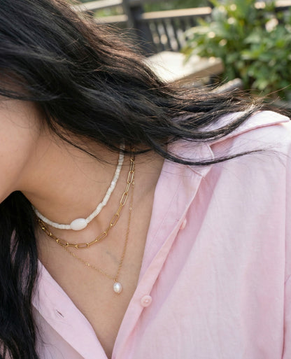 Woman wearing white shell choker layered with gold chain necklaces and pink shirt