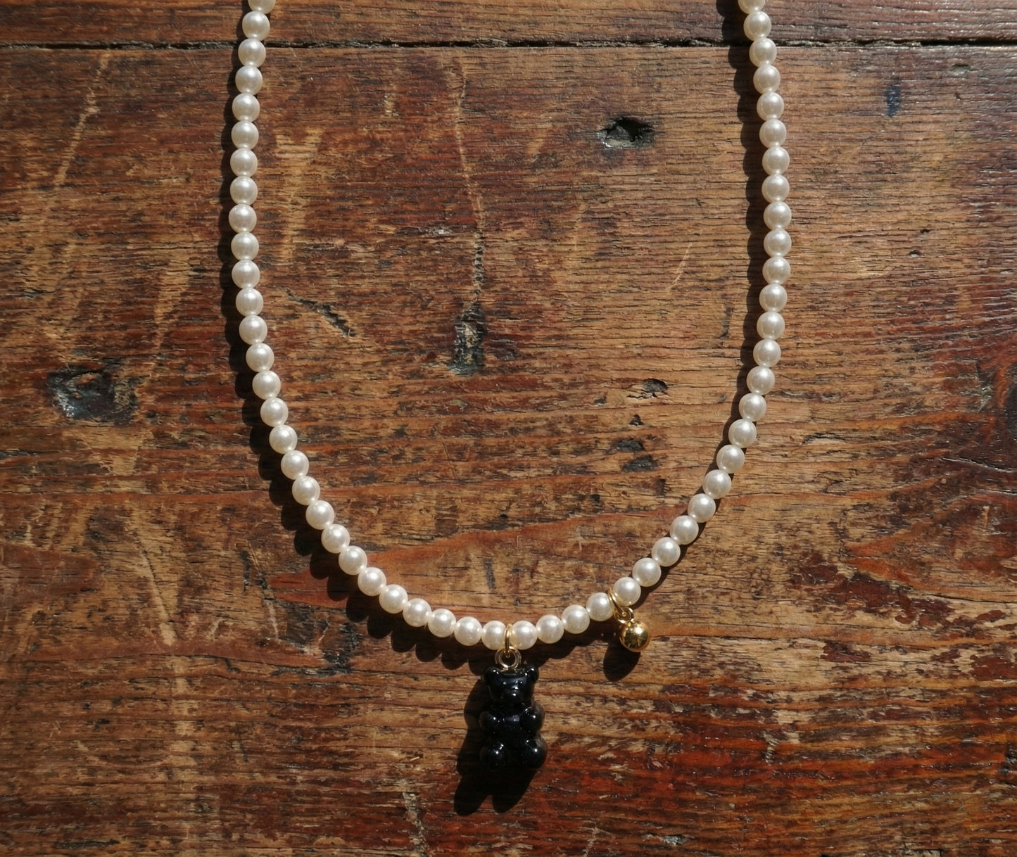 Black gummy bear charm on Swarovski pearl necklace displayed on rustic wood
