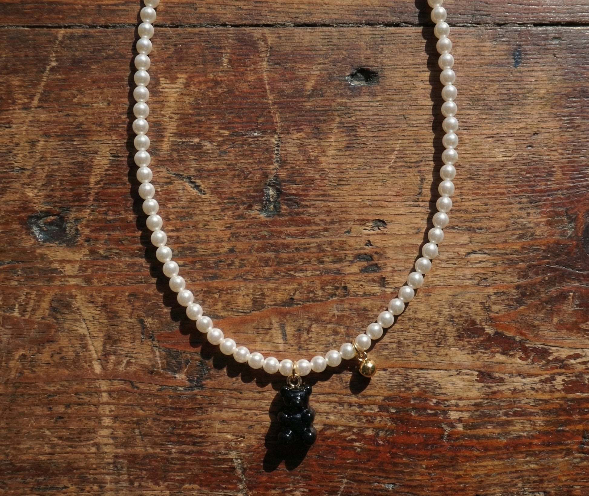Black gummy bear charm on Swarovski pearl necklace displayed on rustic wood