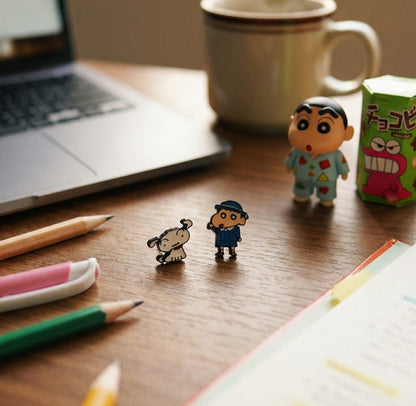Flatlay of school uniform Shin-chan and Shiro earrings on wooden surface with Chocobi snack box and figurines