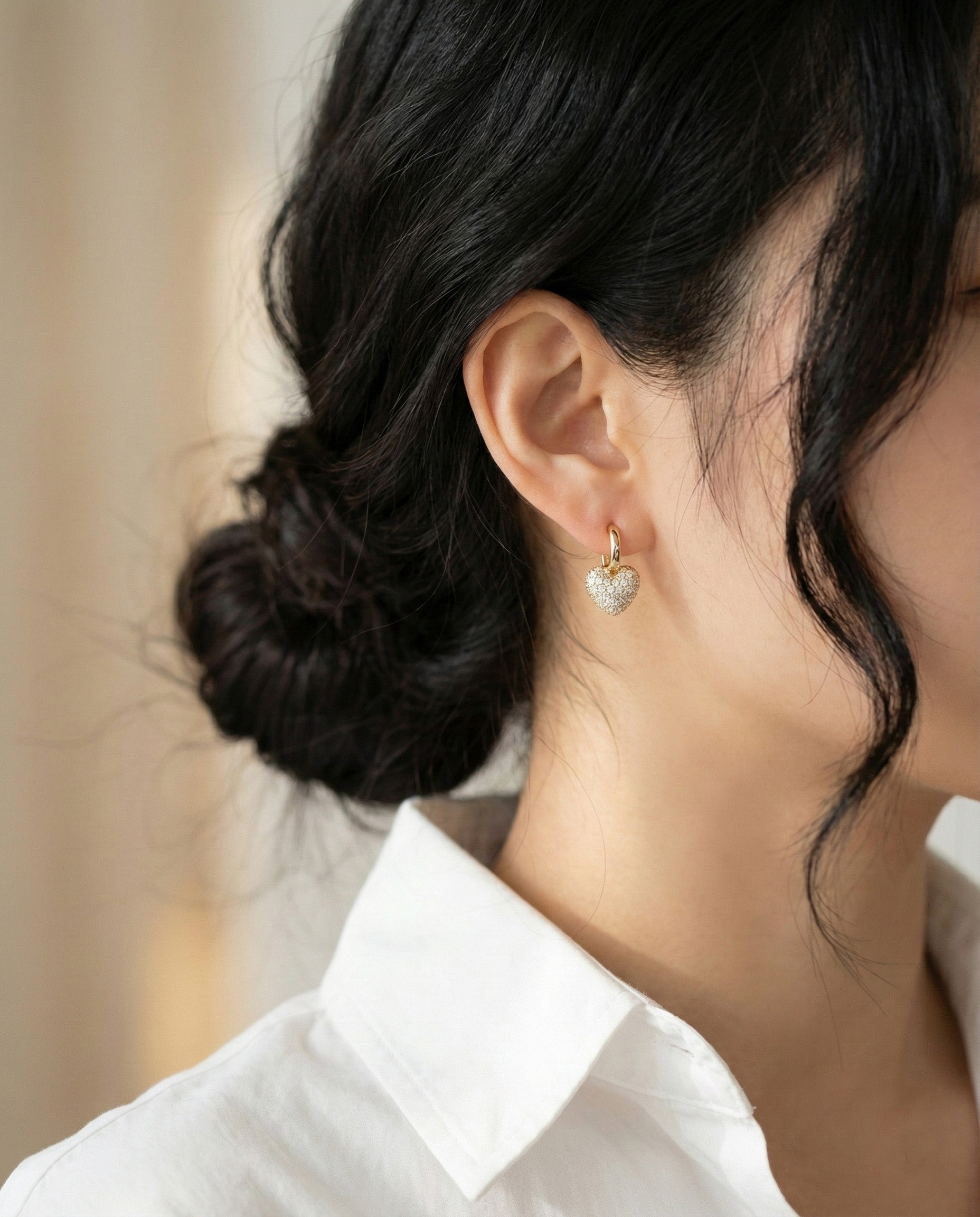 Woman wearing gold pave heart huggie earrings with white shirt elegant everyday jewelry