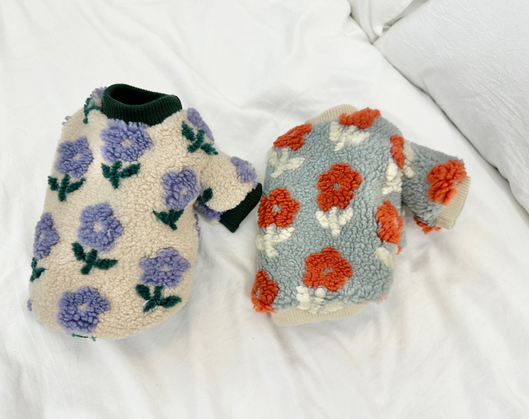 Flat lay of purple and coral floral embroidered dog sweaters on white background