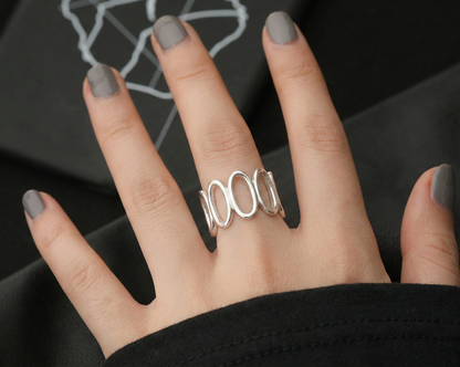 Model wearing oval loop sterling silver wide band ring on middle finger, gray nail polish, dark background with geometric print, modern art jewelry aesthetic