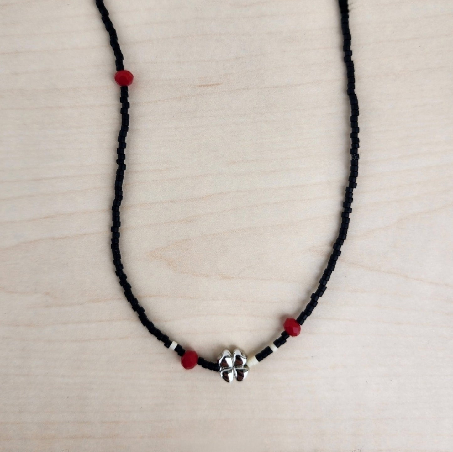 Black seed bead choker necklace with silver four-leaf clover pendant and red beads displayed flat