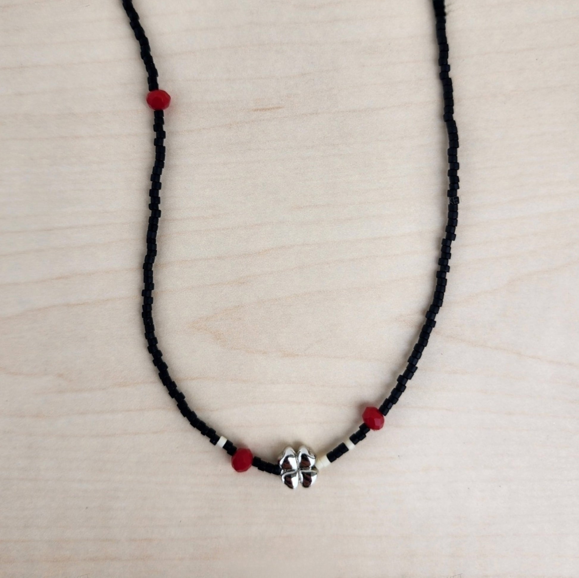 Black seed bead choker necklace with silver four-leaf clover pendant and red beads displayed flat