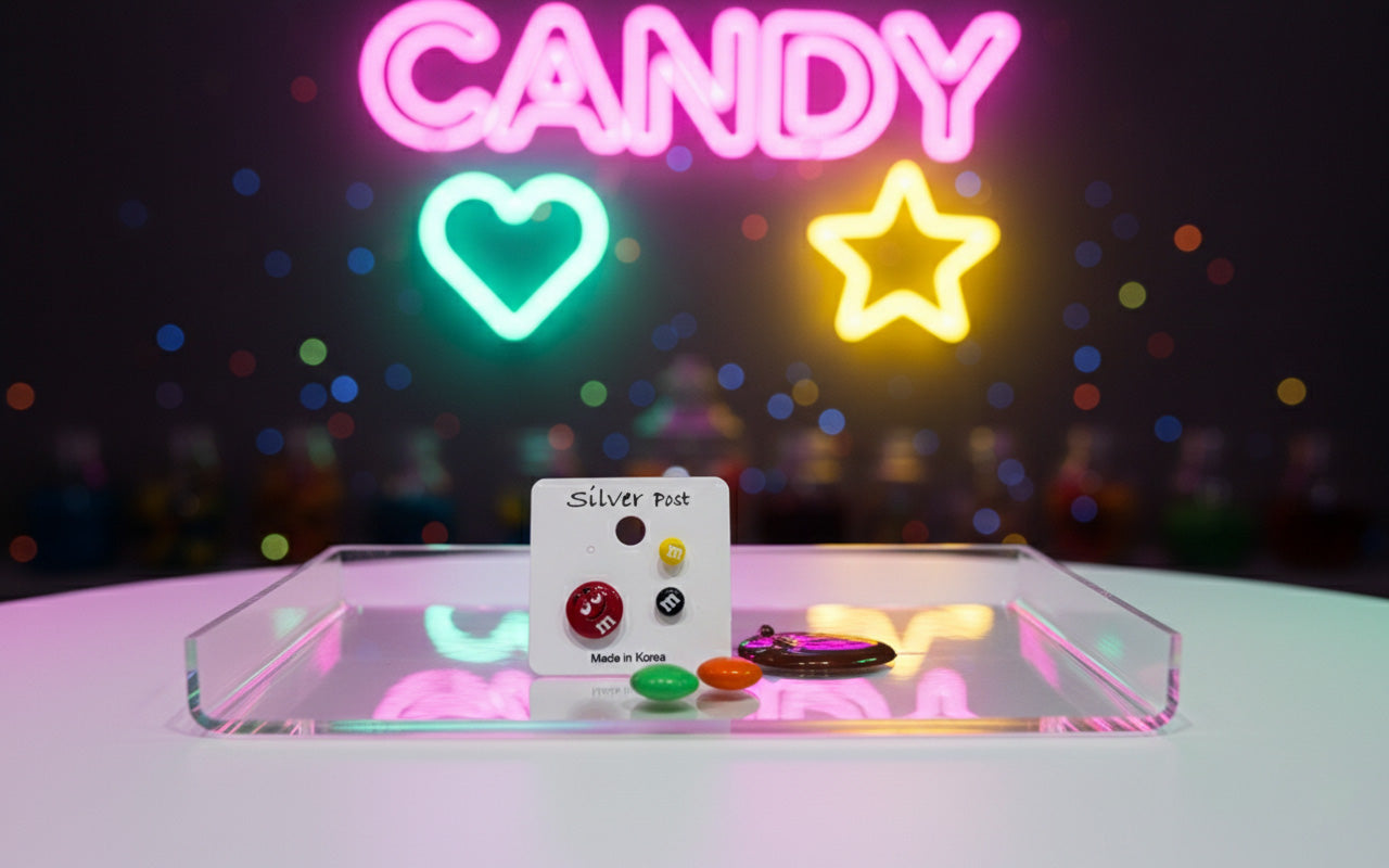 M&M's earring set on clear acrylic tray under pink neon candy sign with glowing heart and star, colorful scattered candies creating vibrant party aesthetic, Korean kawaii jewelry displayed in whimsical sweet shop style