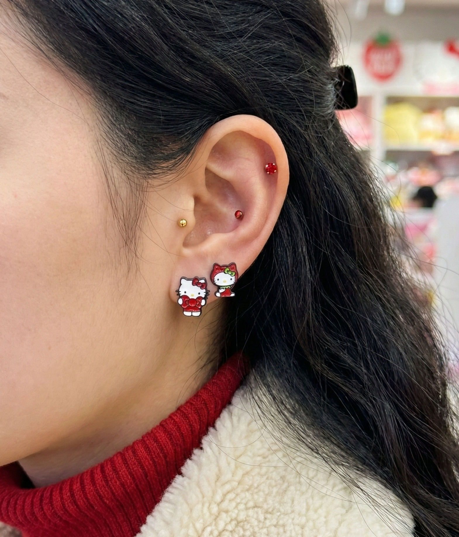Side view of ear wearing red Hello Kitty character earrings with layered piercing look