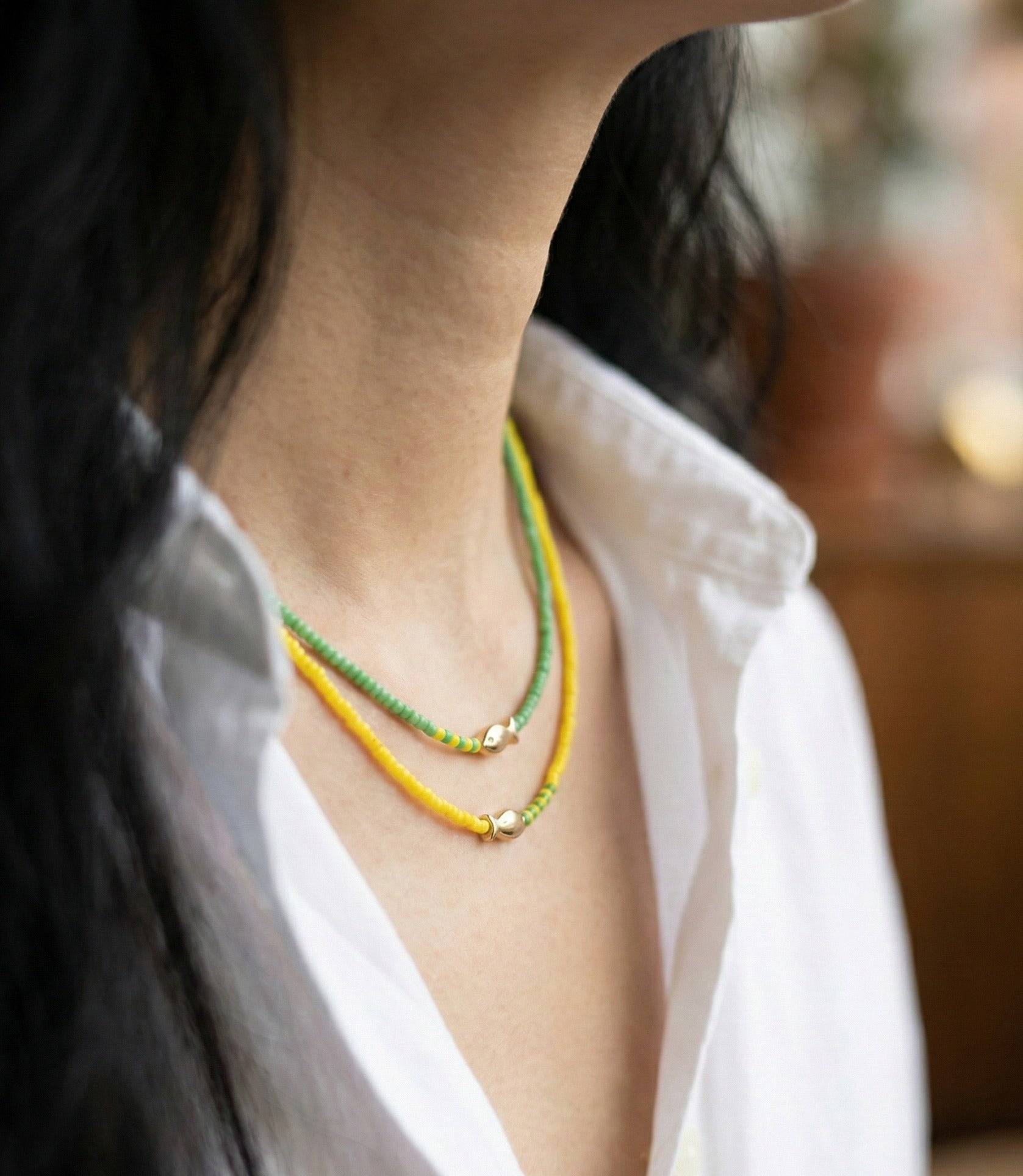  Close-up of woman's neck wearing mint and orange beaded fish necklaces layered look 